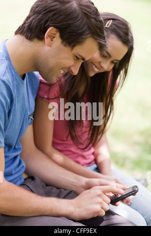 Smiling couple looking at a mobile phone while sitting in a park Stock Photo