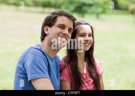 Young smiling man standing in a park with his arm around his girlfriend Stock Photo