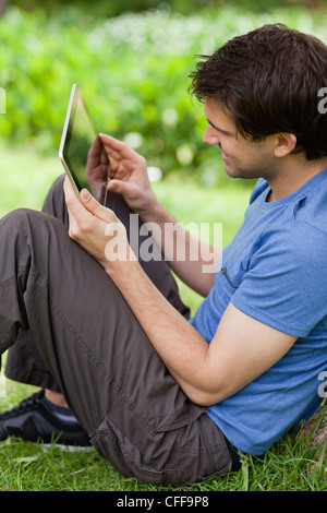 Smiling young man sitting down while using her tablet pc Stock Photo