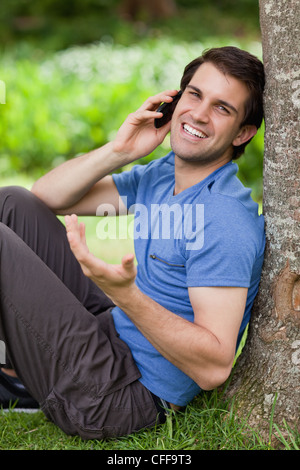 Young happy man talking on the phone while leaning against a tree Stock Photo