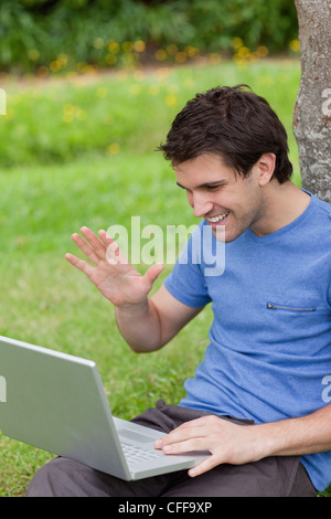 Young smiling man waving his hand in front of his laptop Stock Photo
