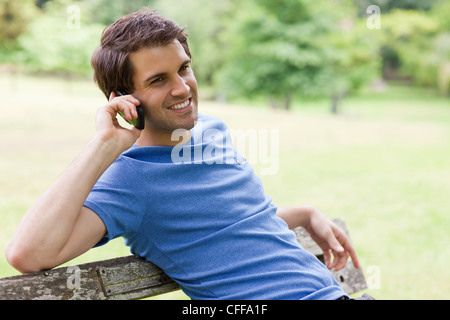 Young relaxed man sitting on a bench while talking on the phone Stock Photo