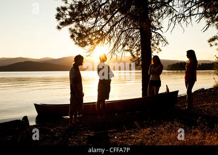 A group of four young adults talking at sunset on a camping trip next to a lake in Idaho. Stock Photo