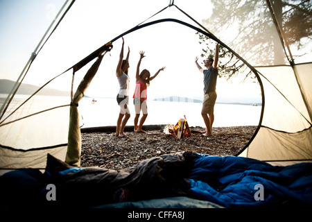 Three young adults smiling and dancing around a camp fire on a camping and kayaking trip on a lake in Idaho. Stock Photo