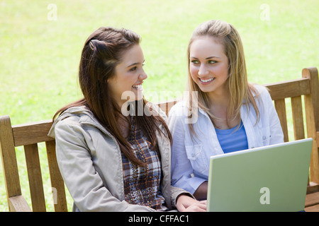 Smiling women sitting on a bench with a laptop on their knees Stock Photo
