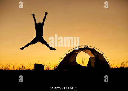 A man jumping next to his tent at sunset on a camping trip in Montana. Stock Photo