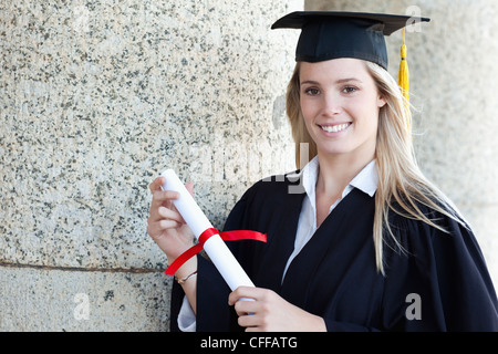 Smiling graduating student wearing a gown while holding her diploma Stock Photo