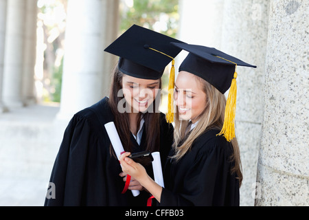 Smiling graduating students looking at a digital camera while standing upright Stock Photo