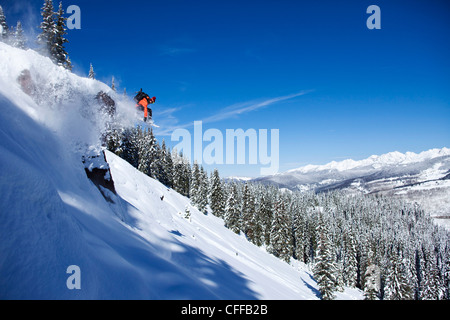 A athletic snowboarder jumping off a cliff on a sunny powder day in Colorado. Stock Photo