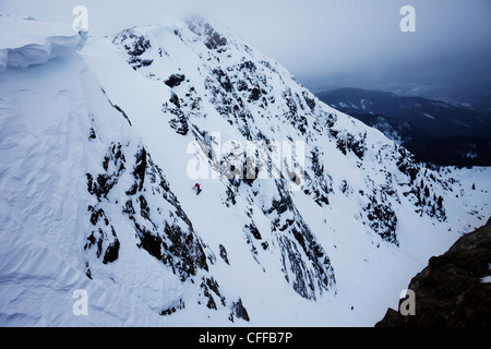 A athletic man snowboarding down a backcountry chute on a stormy day in Colorado. Stock Photo