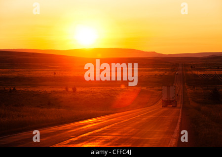 A shipping truck on a long straight highway at sunrise in Montana. Stock Photo