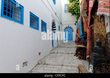 Sidi Bou Said. Tunisia. View of souvenir carpets for sale along narrow cobbled alley with black and white arched blue door at Stock Photo