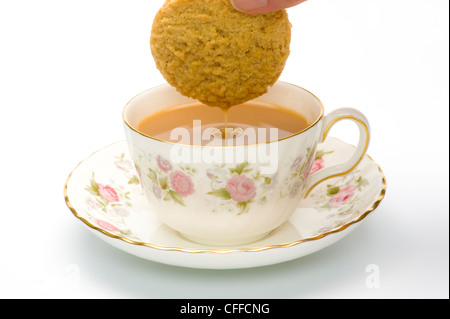 Biscuit dripping with liquid having been dunked into a china cup containing tea. Stock Photo