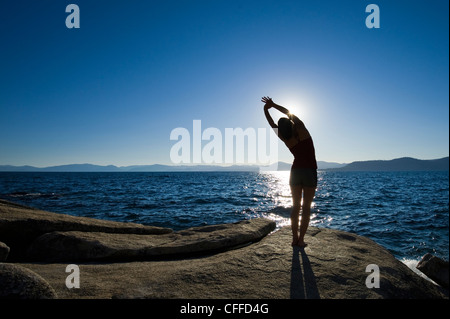 A silhouette of a woman stretching on a granite boulder on the east shore of Lake Tahoe in the summer, NV. Stock Photo