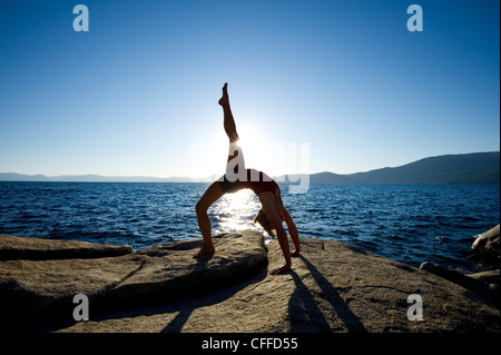 A silhouette of a young woman performing yoga on a granite boulder on the east shore of Lake Tahoe, NV. Stock Photo