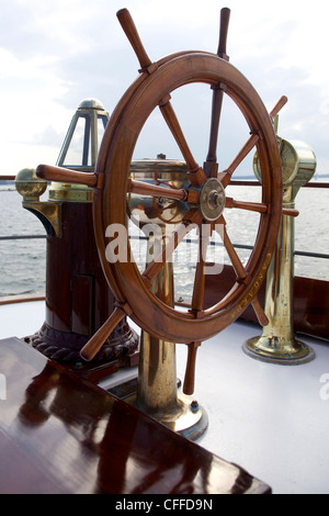 A ship's wheel and compass at the helm of a restored steamship at anchor in Maine. Stock Photo