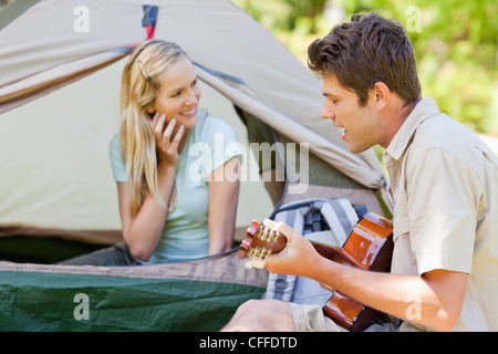 Man sings and plays guitar as his girlfriend smiles Stock Photo