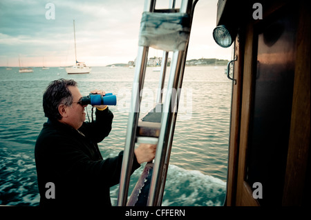 A man looks out through binoculars on a  boat Stock Photo