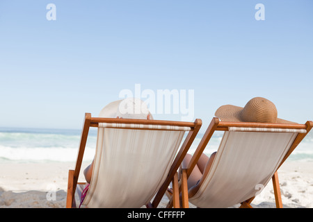 Young women sunbathing while sitting on deck chairs on the beach Stock Photo