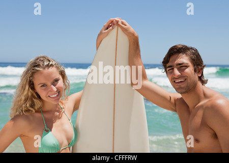Young smiling couple holding a surfboard while crossing their hands Stock Photo