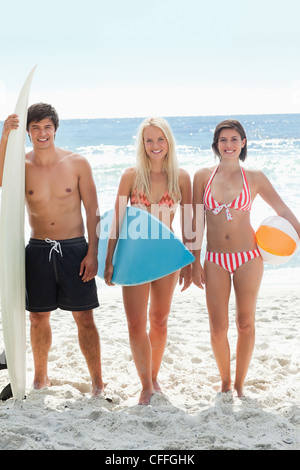 Three friends in swimsuits standing with surfboards and a beach ball Stock Photo
