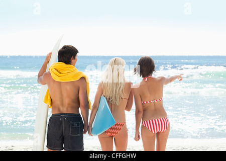 Three friends looking at the sea while pointing Stock Photo
