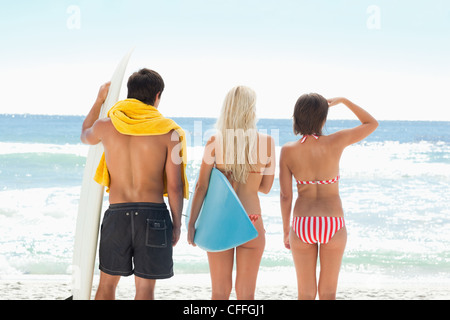 Two women and a man with surfboards at the beach Stock Photo