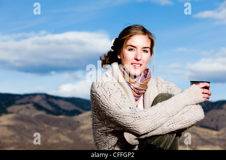A young woman sips coffee and poses in layered outdoor clothing in Fort Collins, Colorado. Stock Photo