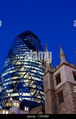 Swiss Re Building 30 St Mary Axe also known as the Gherkin at night with tower of St Andrew Undershaft City Of London England UK Stock Photo