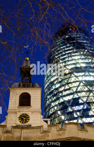 Swiss Re Building 30 St Mary Axe also known as the Gherkin at night with tower of St Helen's Bishopsgate London England UK Stock Photo