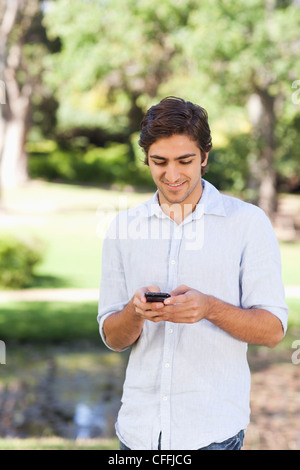 Smiling man using his cellphone in the park Stock Photo