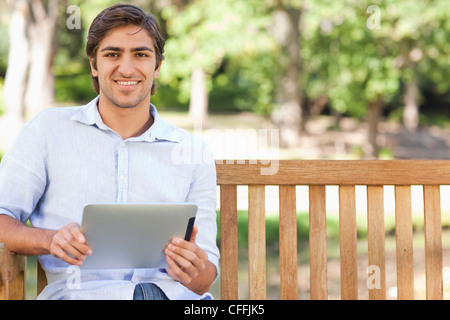 Smiling man with his tablet sitting on a park bench Stock Photo
