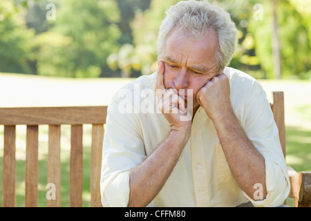 Man holding his face between his hands as he sits on a bench Stock Photo