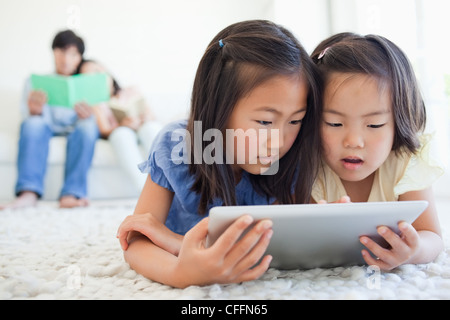 The parents read a book on the couch as the kids use the tablet Stock Photo