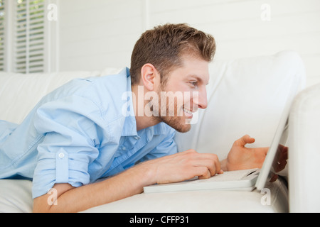 Side view of a man using his laptop while lying across his couch Stock Photo