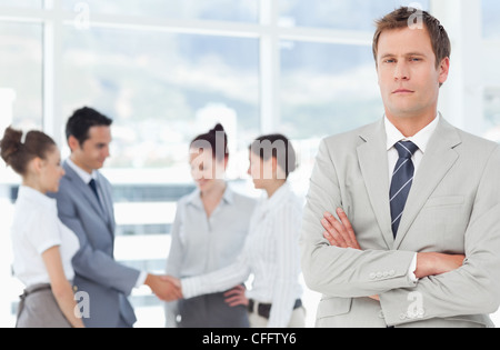 Salesman with arms folded and colleagues behind him Stock Photo