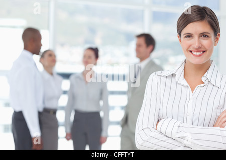 Smiling saleswoman with arms crossed and colleagues behind her Stock Photo