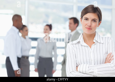 Saleswoman with arms crossed and colleagues behind her Stock Photo