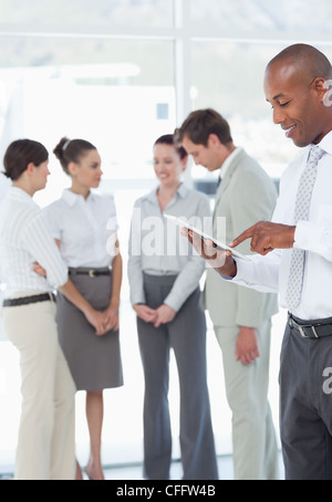 Smiling salesman using his tablet computer with colleagues behind him Stock Photo