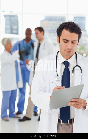 Young doctor taking notes with colleagues behind him Stock Photo