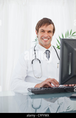 Smiling doctor working on his computer while sitting at a desk Stock Photo