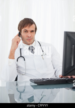 Thoughtful doctor talking on his mobile phone while raising an eyebrow Stock Photo