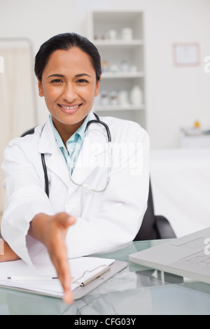 Smiling doctor offering a handshake while sitting at her desk Stock Photo