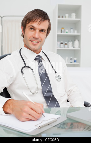 Smiling doctor looking at the camera while writing on his clipboard Stock Photo