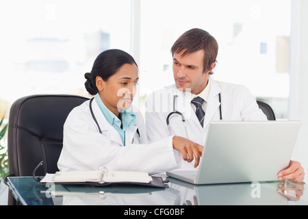 Serious doctor pointing at the screen of the laptop while talking to her colleague Stock Photo