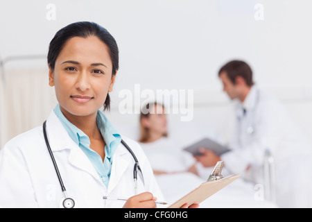 Attractive doctor writing on her clipboard while standing in a hospital room Stock Photo
