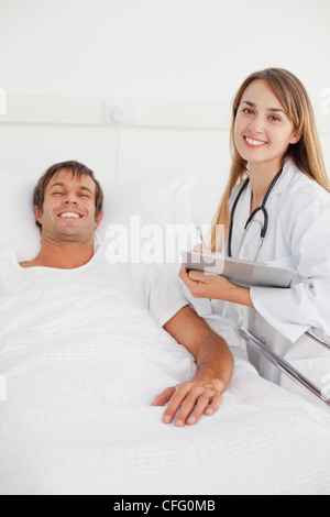 Smiling doctor standing next to a hospital bed while holding a clipboard Stock Photo