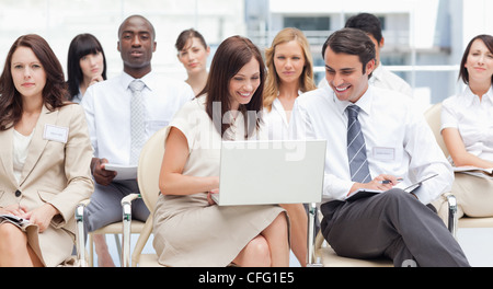 Two colleagues look at a laptop as they sit in a group Stock Photo