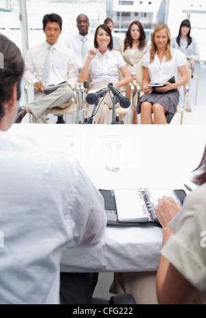 Business team watching two colleagues sitting behind a tablet Stock Photo