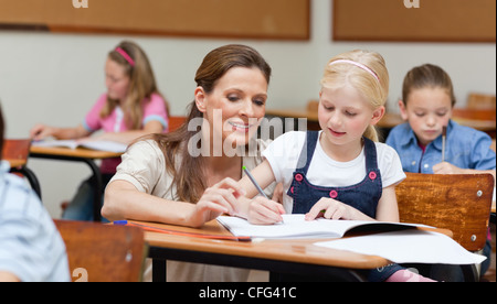 Primary school teacher helping a girl writing at her desk Stock Photo ...